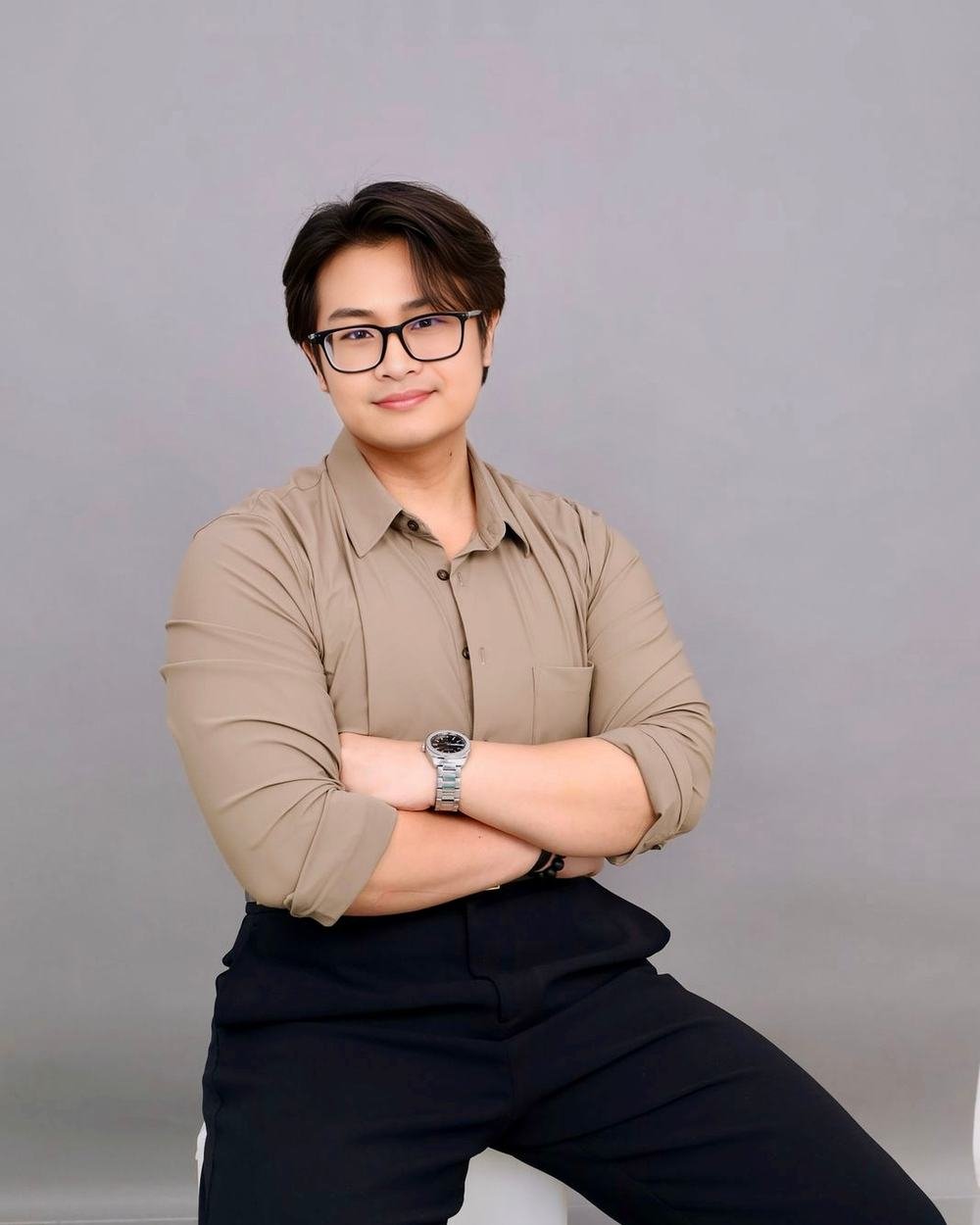 Portrait of Adha Gozali in a tan shirt, arms crossed, against a grey backdrop.