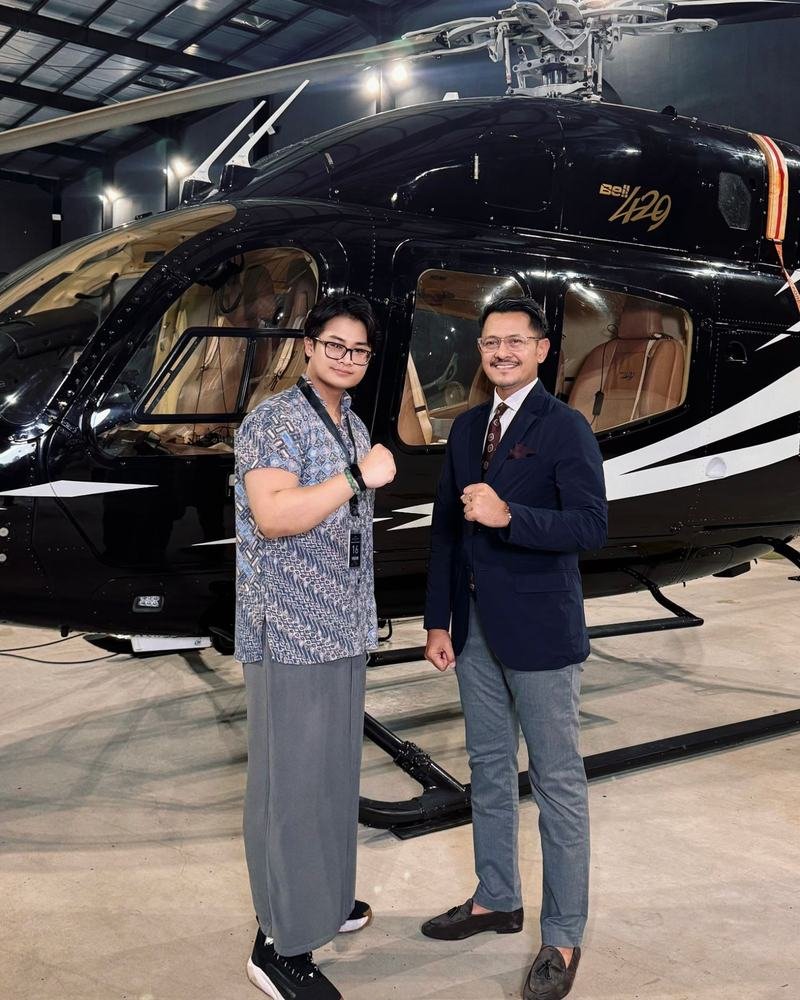 Adha Gozali with Denon Prawiraatmadja beside a Bell 429 helicopter in a hangar.