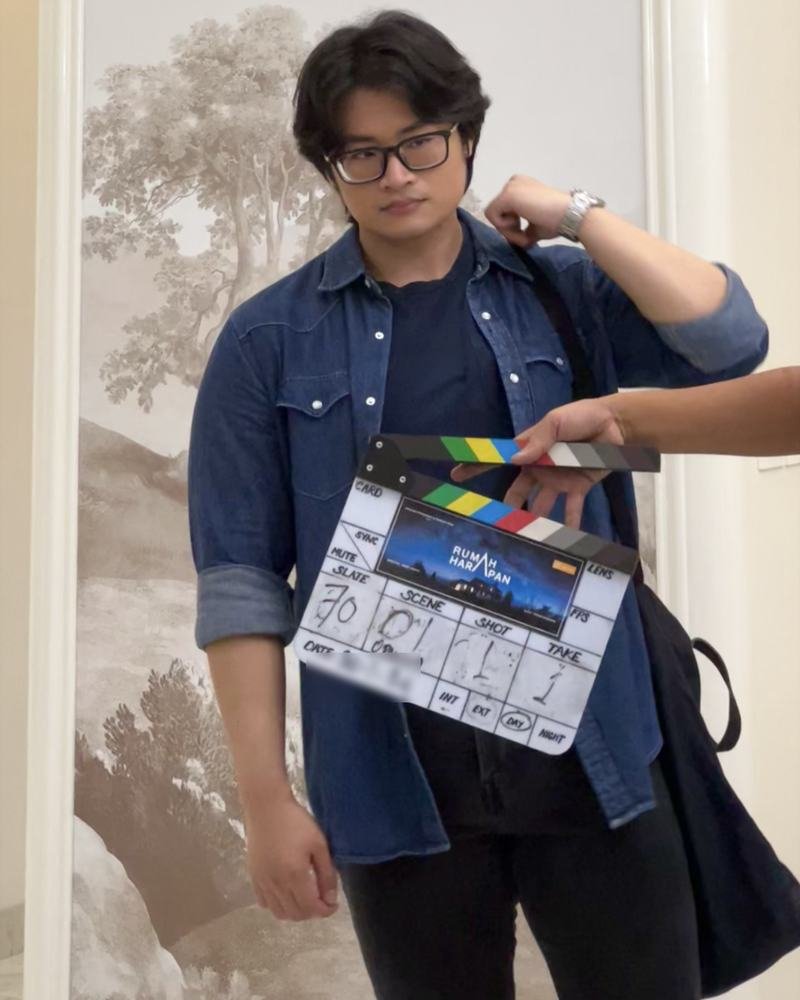 Adha Gozali on the set of Rumah Harapan, a clapperboard held up in front of him.